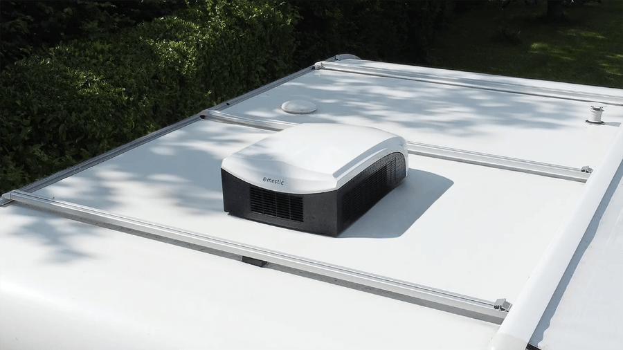 White Mestic RTA-2500L rooftop air conditioner installed on a caravan roof in an outdoor setting.