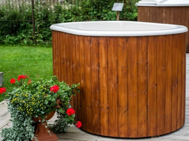 Viking Industrier Ofuro hot tub with white fiberglass interior and dark brown wooden exterior, next to a potted red flower.