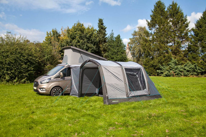 Side view of the Outdoor Revolution Cayman Air T3 Lite driveaway awning attached to a campervan on a grassy campsite with trees and bushes.