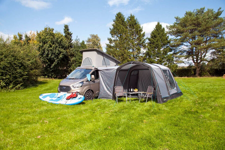 ngled front view of the Outdoor Revolution Cayman Air T3 Lite driveaway awning attached to a campervan on a grassy campsite with camping chairs and a table set up