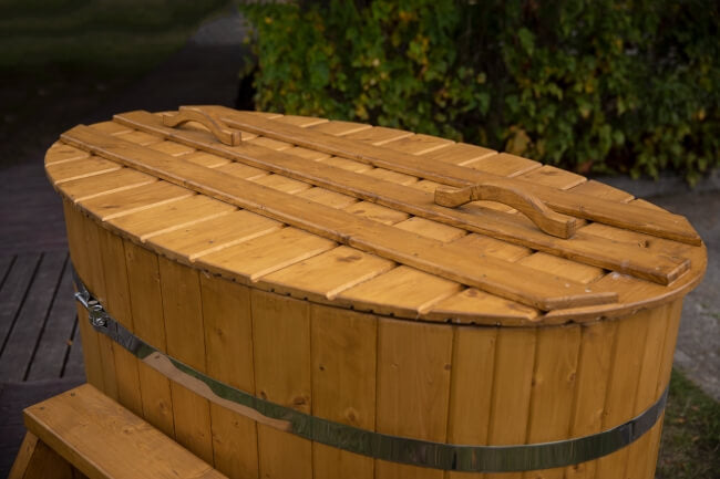 Viking Industrier oval wooden cold tub with matching wooden lid and handles, placed outdoors on a wooden deck, surrounded by green bushes.