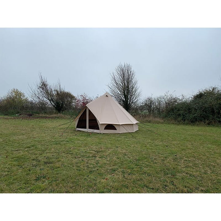Side view of Quest Leisure Signature 4M Classic Bell Tent pitched on green grass with bare trees in the background.