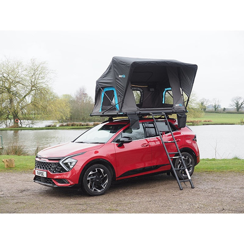 Skypod Rapide rooftop tent mounted on a red SUV with ladder access, set up beside a lake.