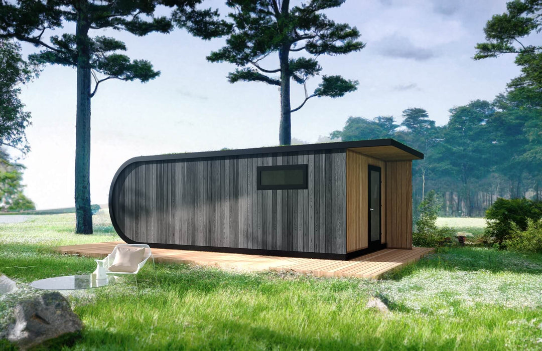 Modern glamping pod with dark wood cladding and wooden porch, placed on a deck surrounded by lush forest grass.