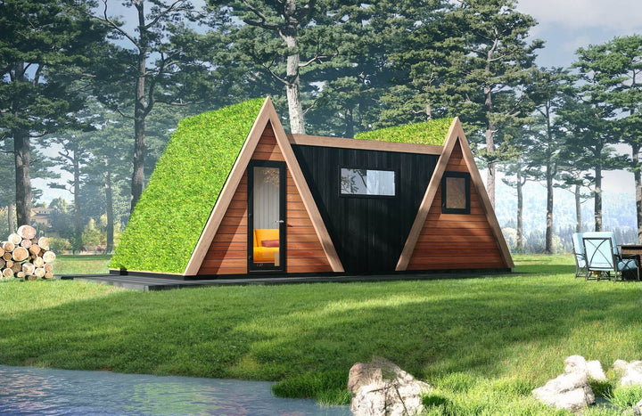 Lakeside A-frame duo glamping unit with green living roofs and black timber center, set among pine trees with firewood stack and outdoor dining.