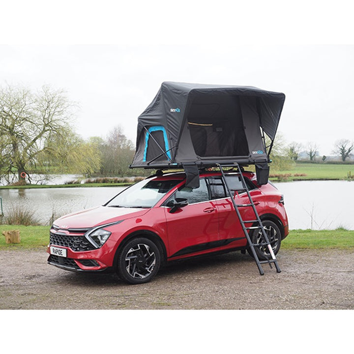 Skypod Rapide rooftop tent mounted on a red SUV with ladder access, set up beside a lake.