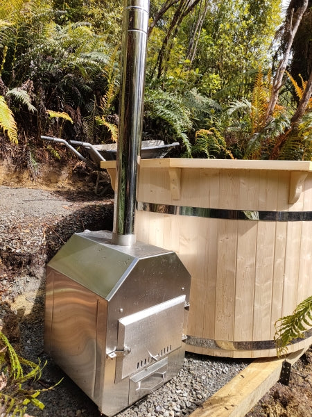 Close-up side view of Viking Industrier Spruce hot tub with stainless steel external heater, placed in a forest setting on gravel ground.