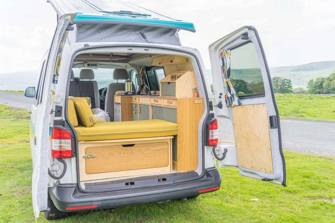 Campervan Squall Kitchen Unit rear view showing bench seat and complete kitchen setup inside a white campervan, countryside background.