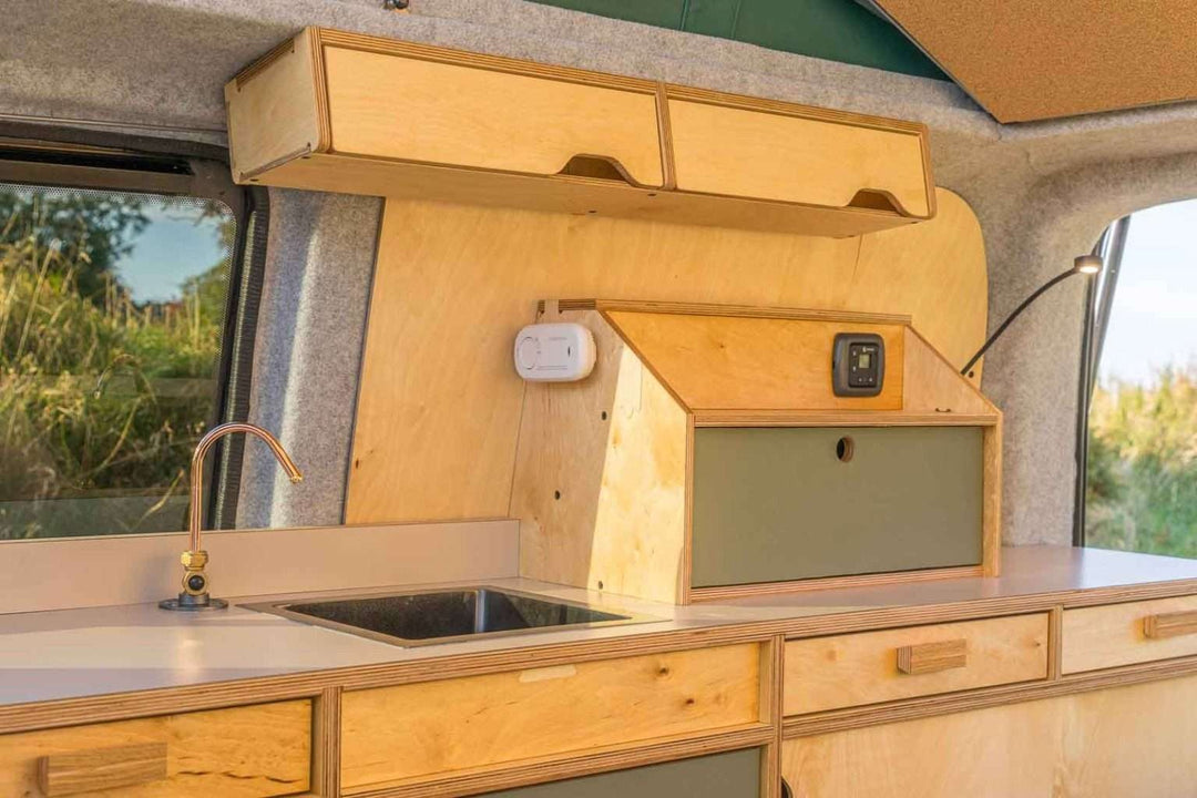 Campervan Squall Kitchen Unit detailed cabinet and drawer storage with hob and sink, countryside visible through windows.