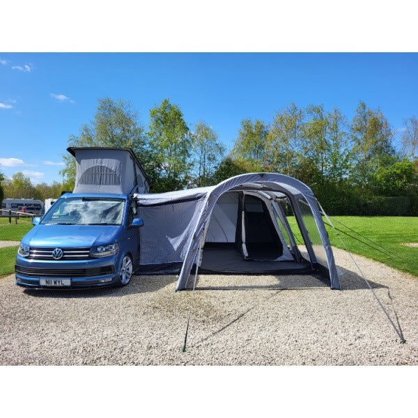 Blue Volkswagen campervan with Sunncamp Touring Motor Air Driveaway Awning attached on gravel pitch with grass surroundings