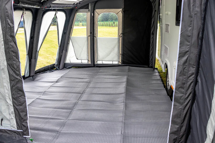 Sunncamp Awning Carpet grey flooring laid inside an awning beside a caravan on a grass field.