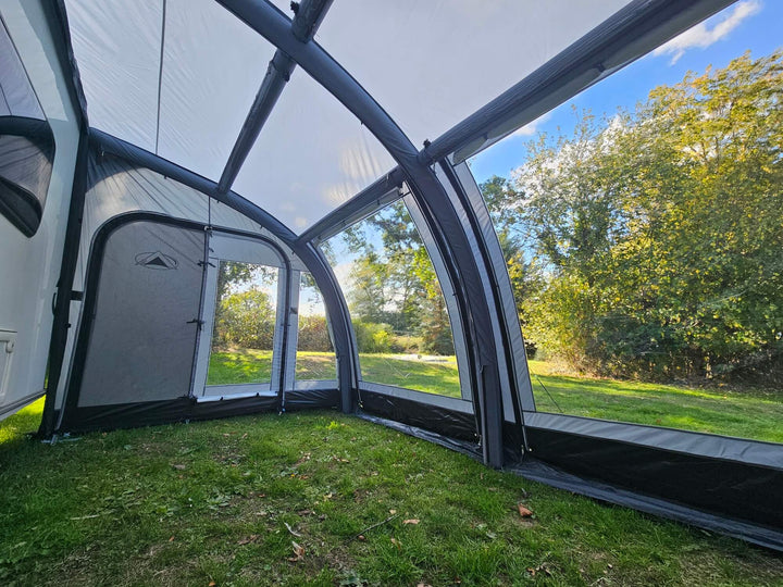 Interior view of the Sunncamp Ultima Versara Air 390 Deluxe Porch Awning showing inflatable frame structure and large windows with trees and grass visible outside.