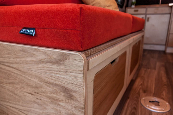 Campervan “Swale” Benches angled close-up of red upholstered seat cushion and oak ply storage base with Contour label inside campervan.