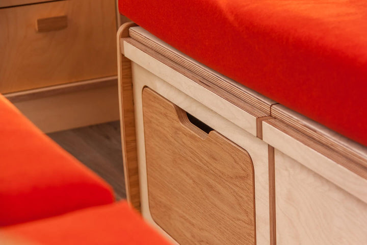 Campervan “Swale” Benches close-up of oak plywood storage drawer with recessed handle beneath red cushion inside campervan.