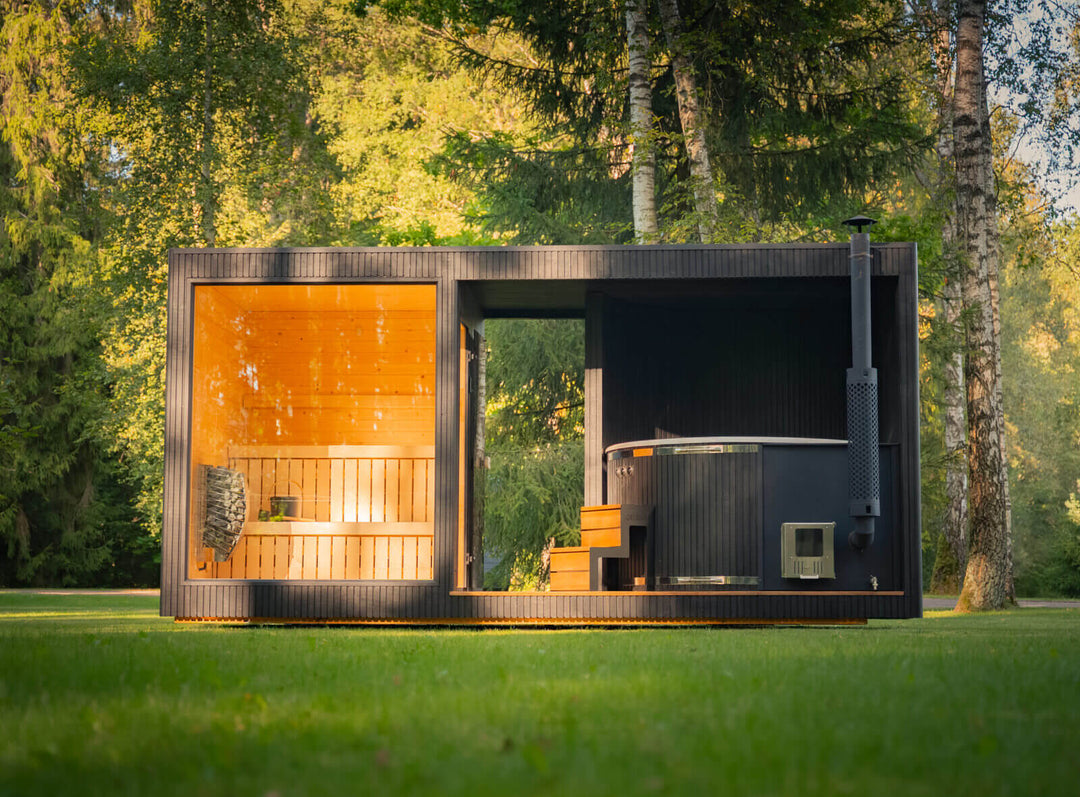 Taurus Classic Outdoor Sauna full front view with large glass sauna window and round hot tub section set on grass in a forest environment.