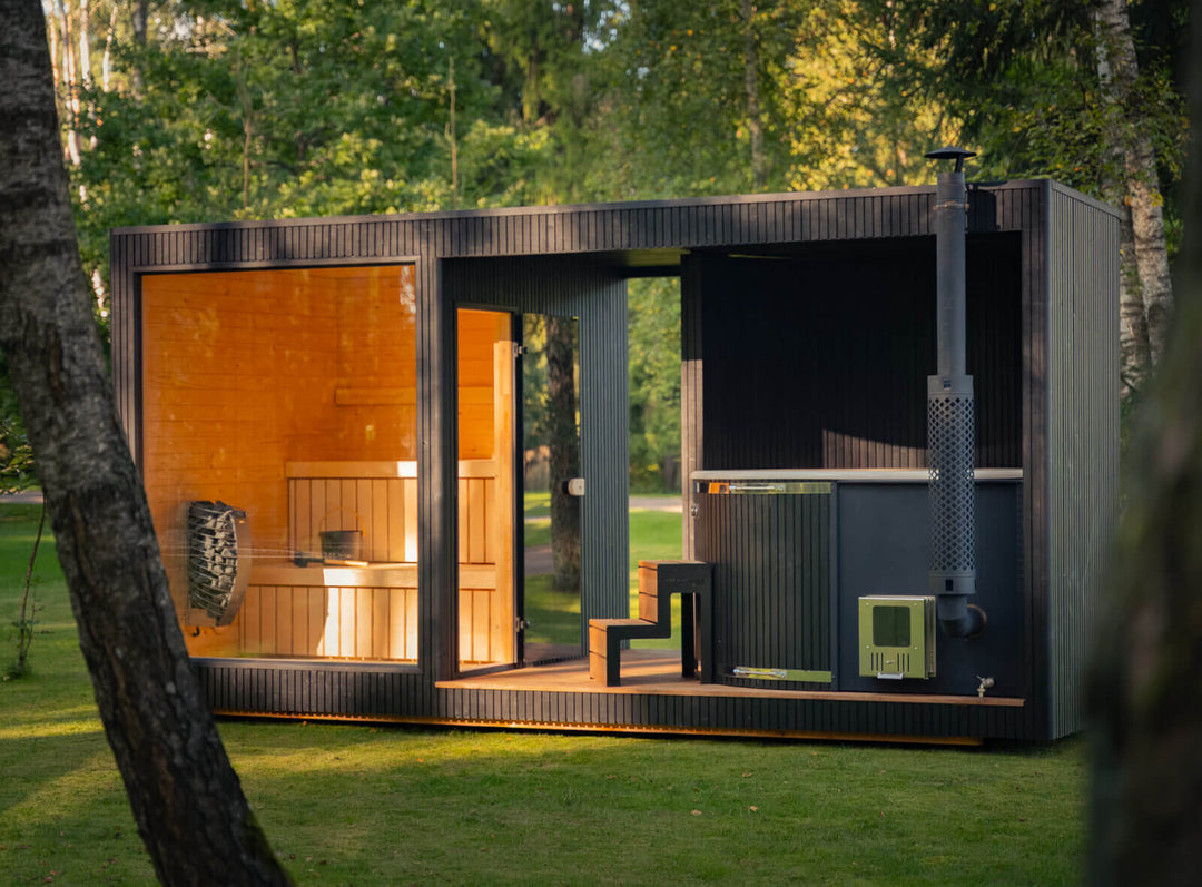 Taurus Classic Outdoor Sauna exterior view with illuminated sauna interior and integrated hot tub in a green park.