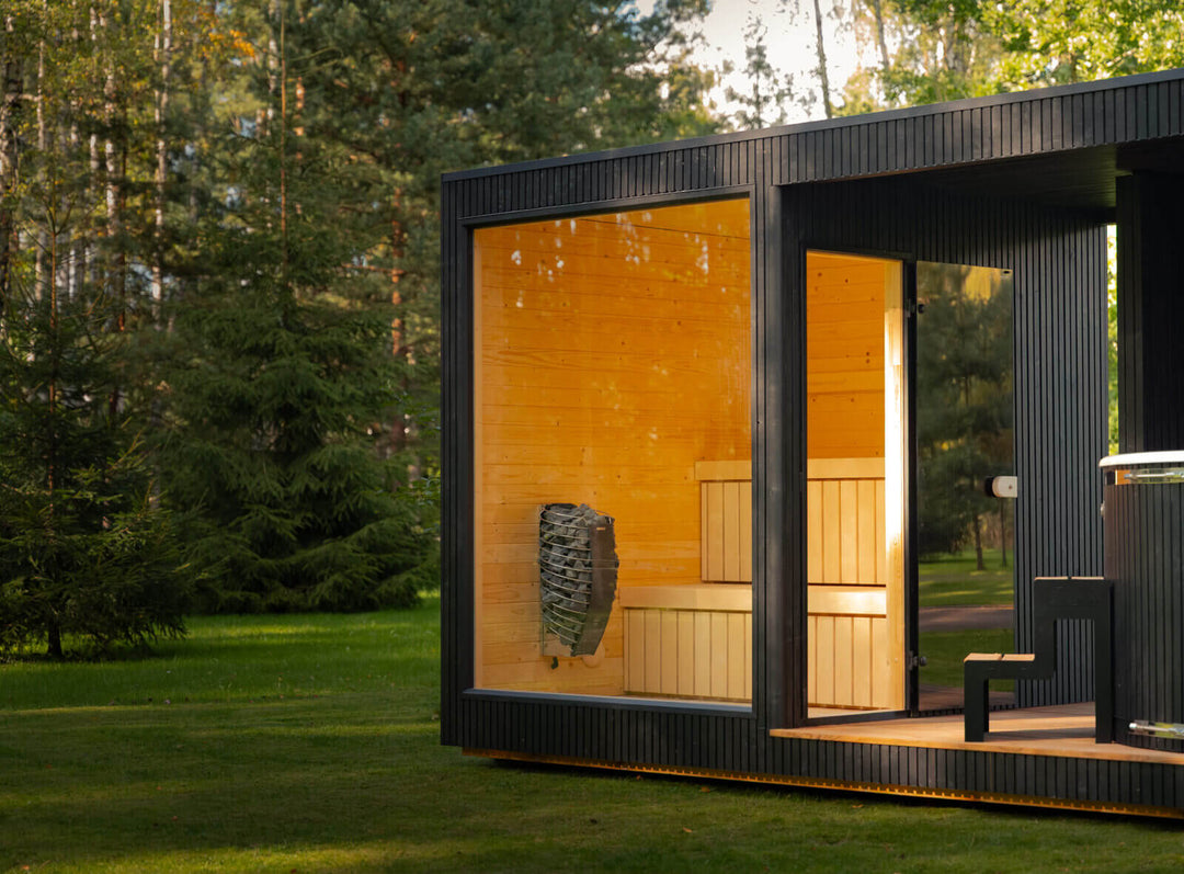 Taurus Classic Outdoor Sauna showing glass-front sauna room and outdoor hot tub area surrounded by a forest landscape.