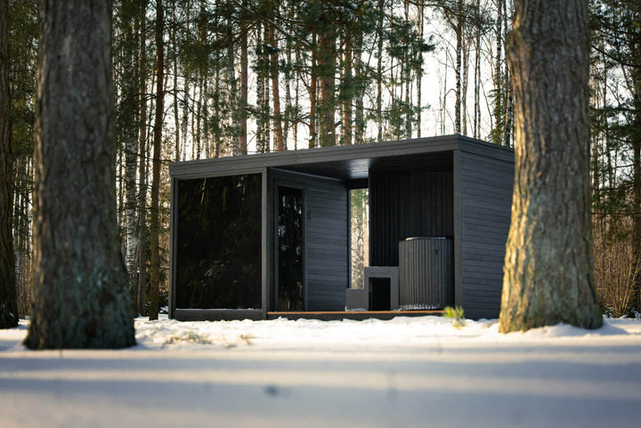 Taurus Modular Air Outdoor Sauna modern rectangular design with glass wall and sheltered area shown in a snowy forest background.