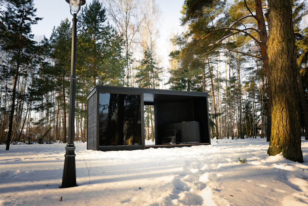Taurus Modular Air Outdoor Sauna installed in a snowy forest setting with tall pine trees and warm sunlight in the background.