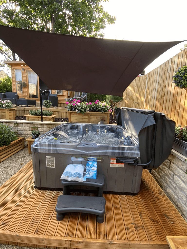 Front view of Luso Spas The Hawaii 2 Hot Tub on a wooden deck under a canopy with towels and spa chemicals on the steps.