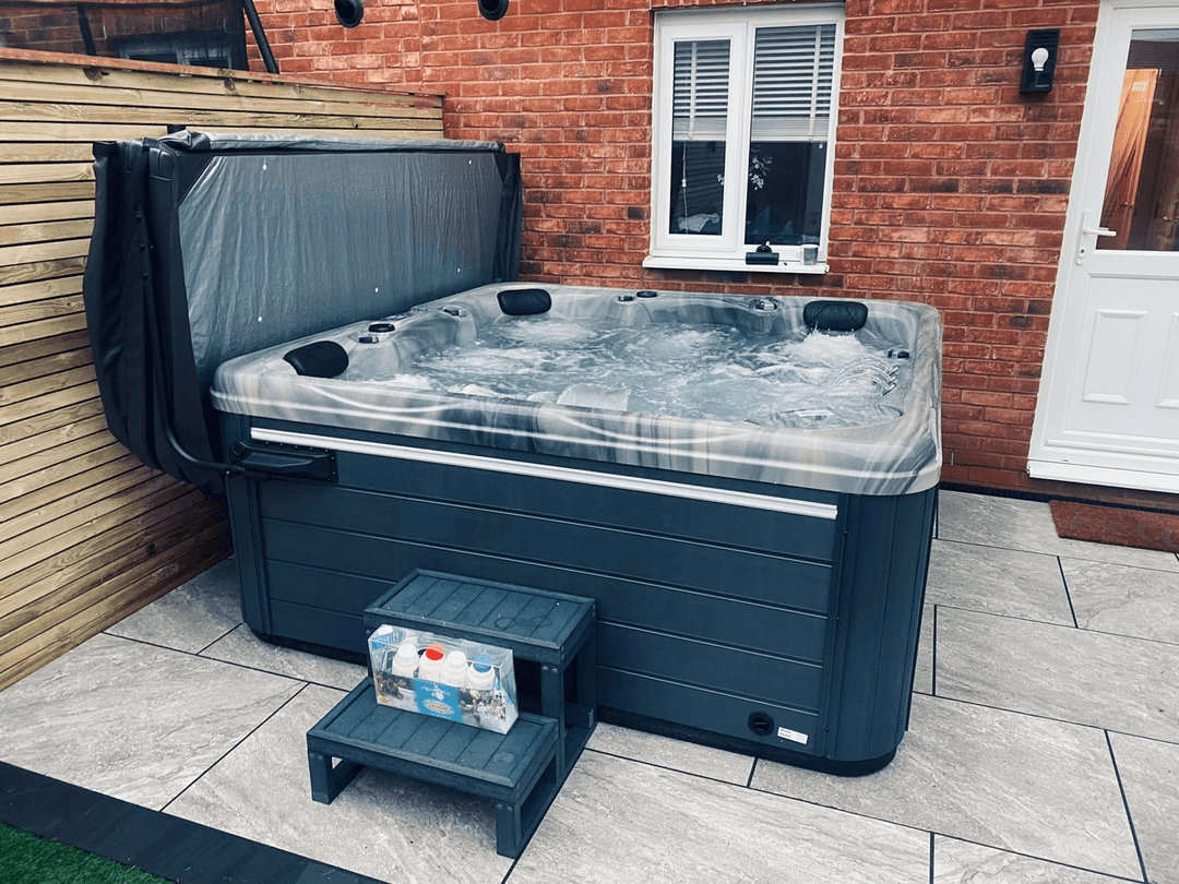Luso Spas The Luna Hot Tub with marble-effect shell and water bubbling beside a brick house.