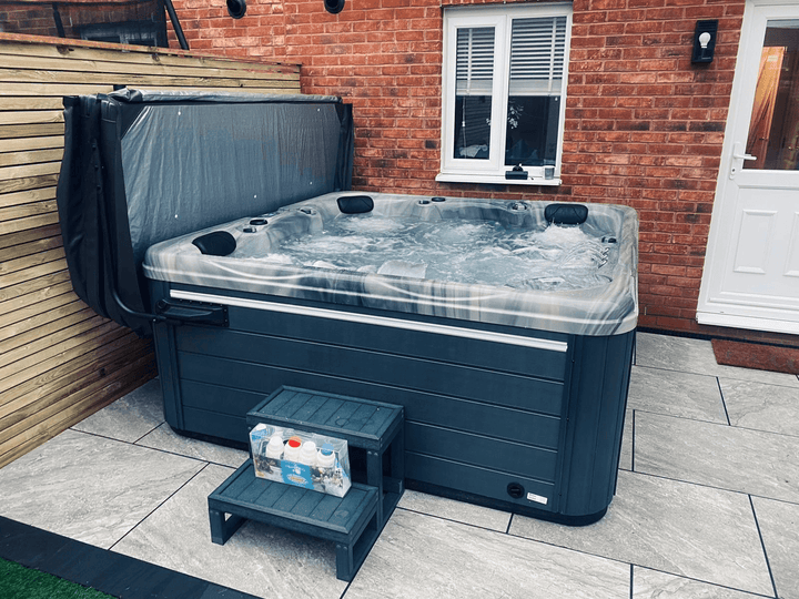 Luso Spas The Luna Hot Tub with marble-effect shell and water bubbling beside a brick house.