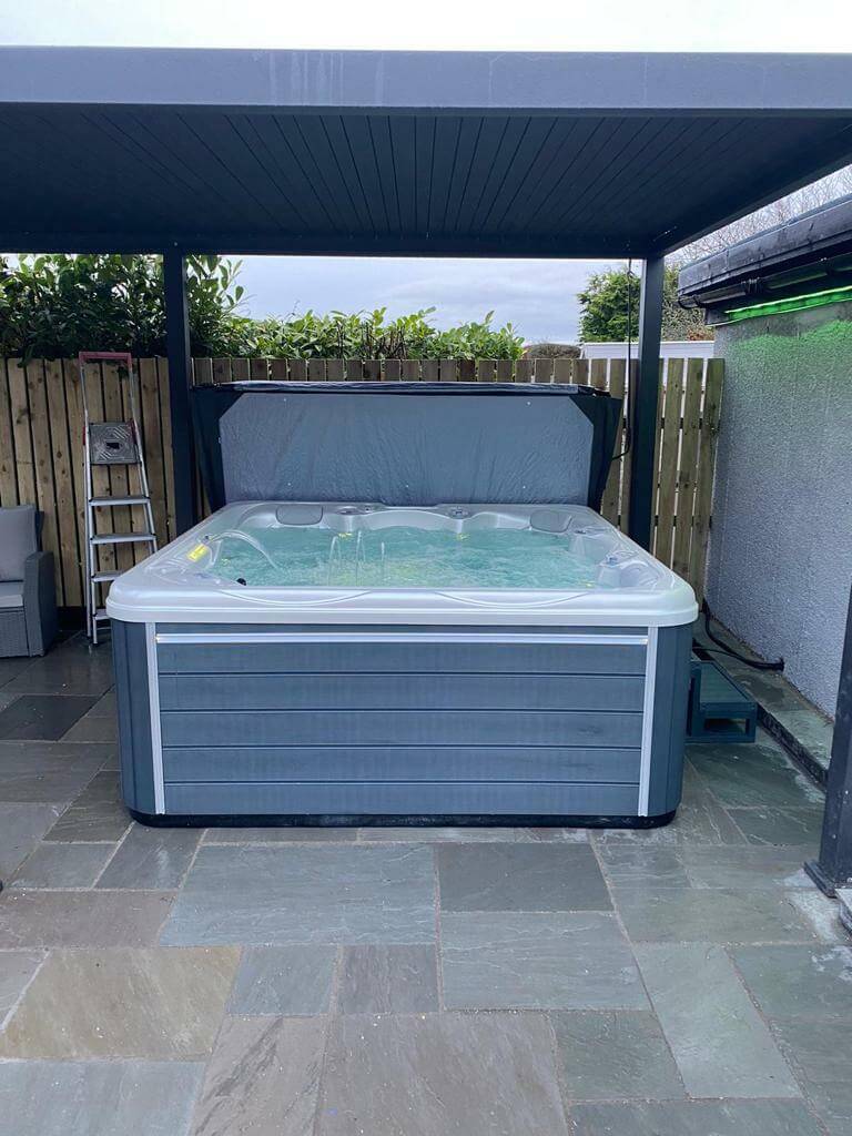 Luso Spas The Luna Hot Tub filled with water under a pergola on a stone patio.