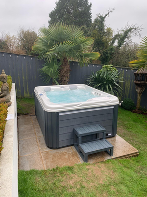 Luso Spas The Vepo Hot Tub placed in a backyard garden with steps and tropical plants surrounding it.