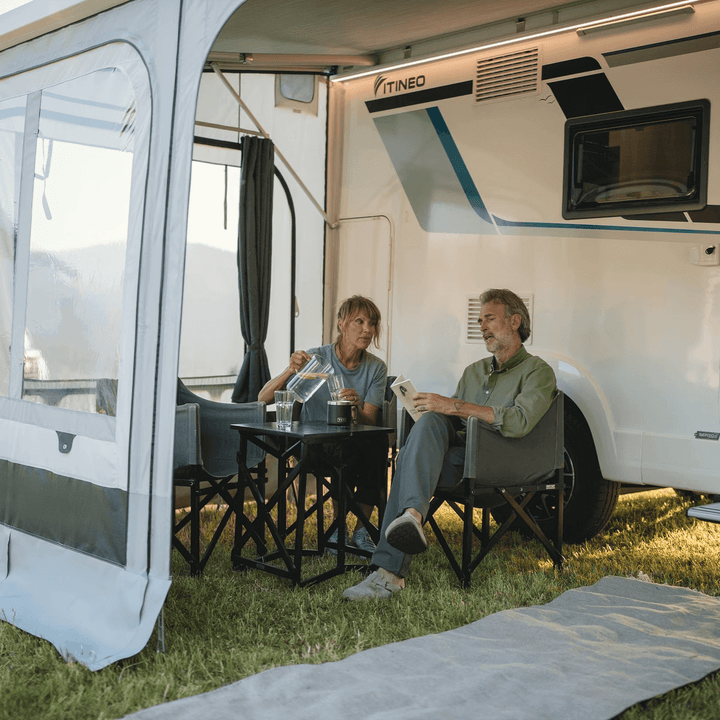 Couple relaxing inside an awning room with Thule curtains fitted, on a grassy campsite.