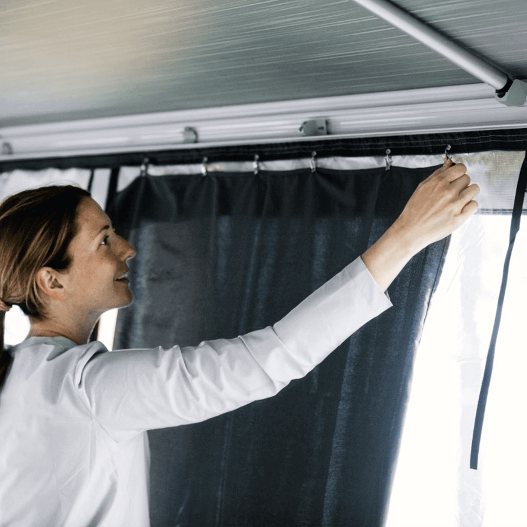 Person fitting Thule awning curtains inside an awning room at a campsite with.
