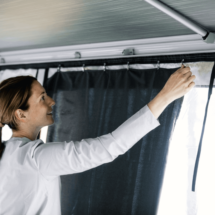 Person fitting Thule awning curtains inside an awning room at a campsite with.