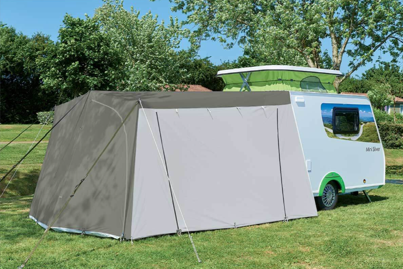 Gray mini silver tent attached to a caravan on grass with trees in the background