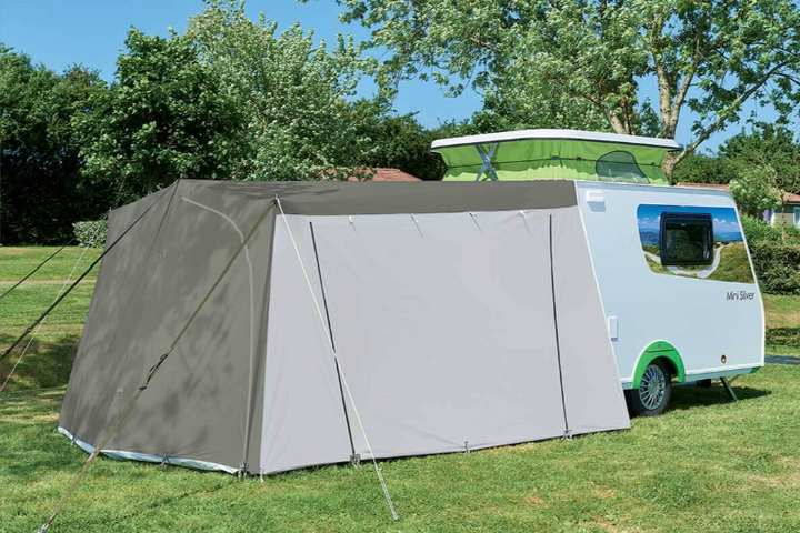Gray mini silver tent attached to a caravan on grass with trees in the background