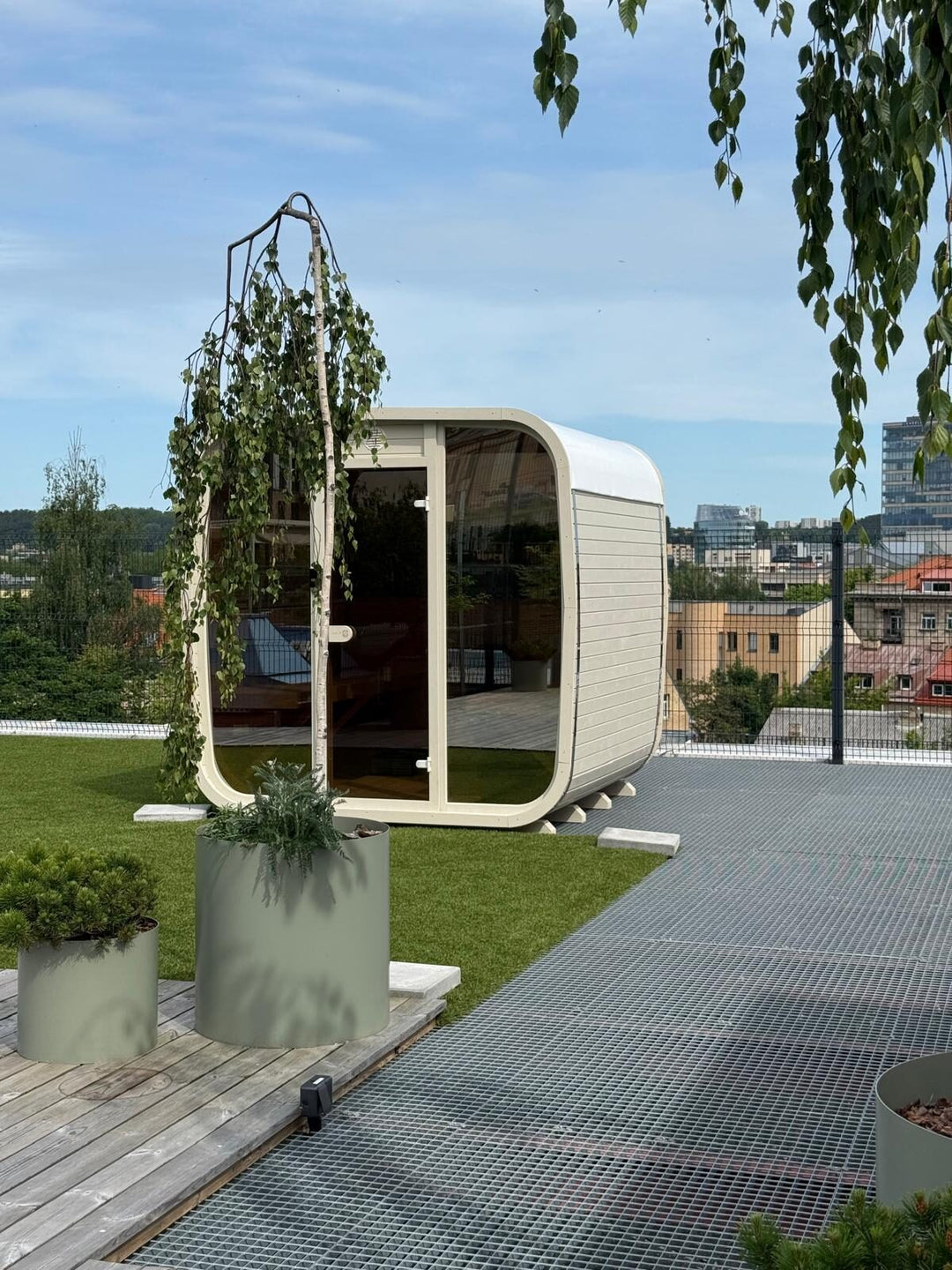 Ula Classic Outdoor Sauna in light finish installed on a rooftop terrace with city buildings and greenery in the background.