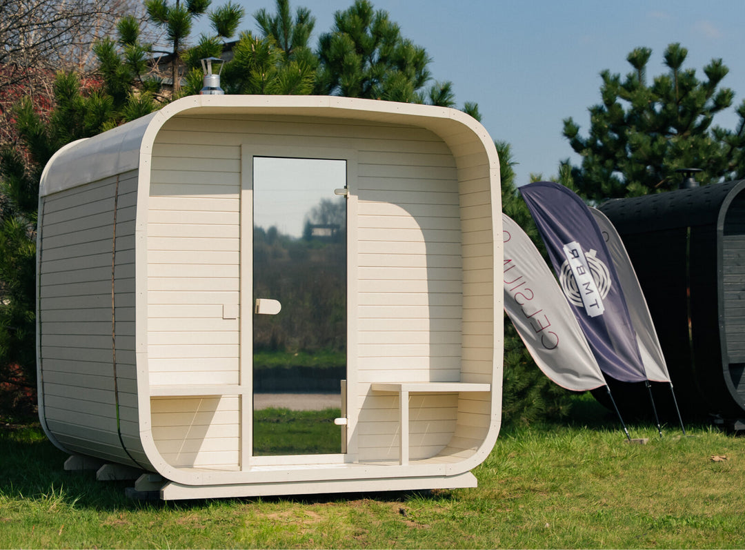 Ula Grand Outdoor Sauna in hazel finish installed on grass in an outdoor setting with trees and branded flags in the background.