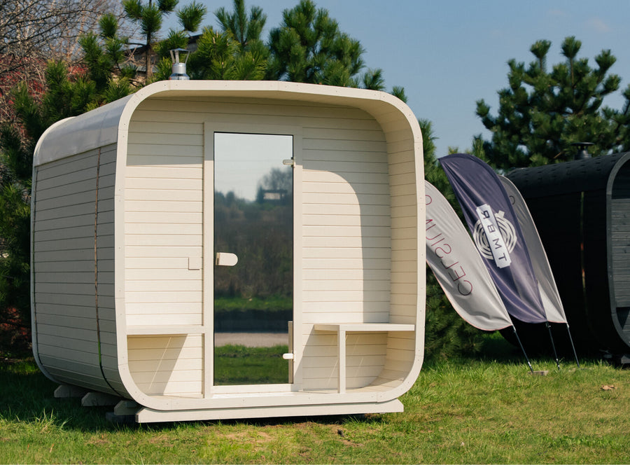Ula Grand Outdoor Sauna in hazel finish installed on grass in an outdoor setting with trees and branded flags in the background.