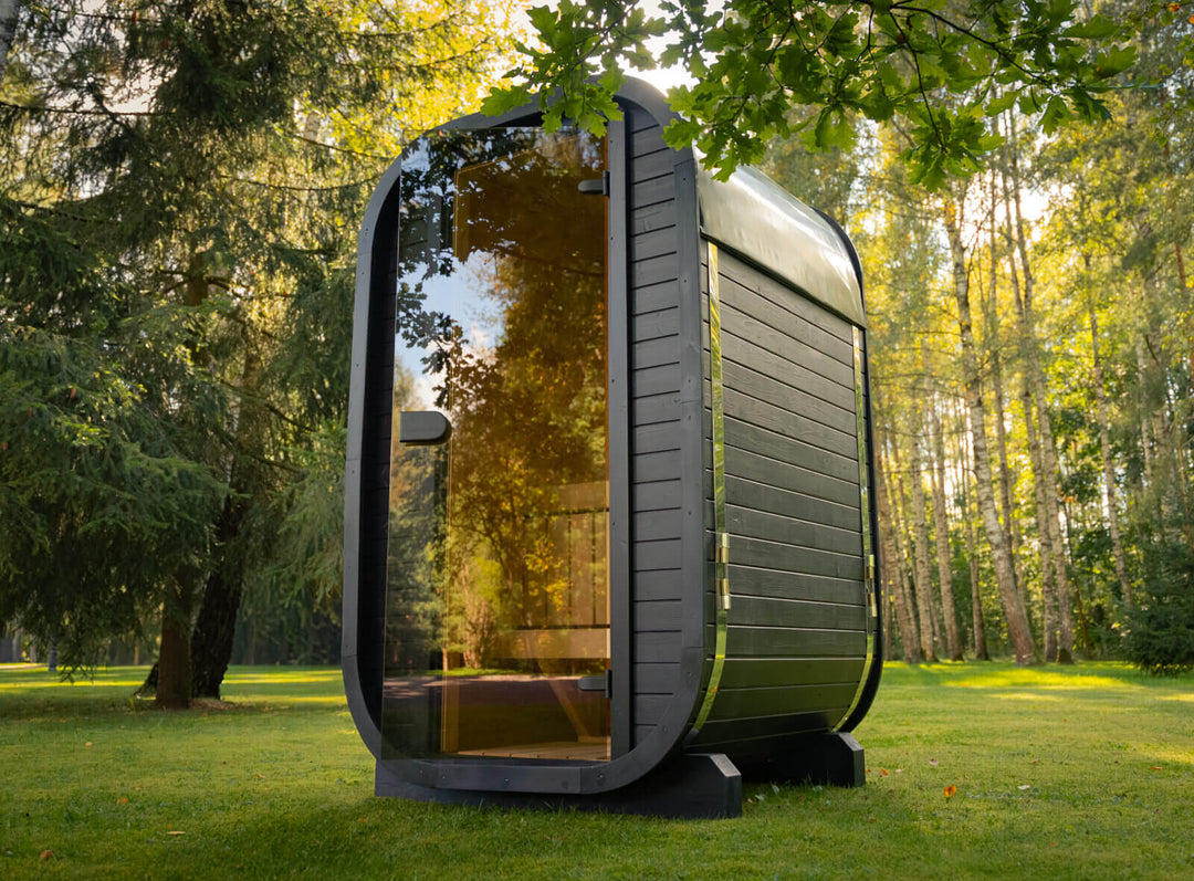 Ula Micro 2-Person Outdoor Sauna black exterior sauna with tinted glass door placed on grass in a forest garden background.