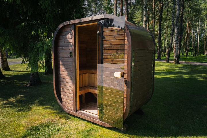 Ula Mini Outdoor Sauna 2 person wooden barrel-style sauna with glass door set in a forest garden on a grassy lawn background.