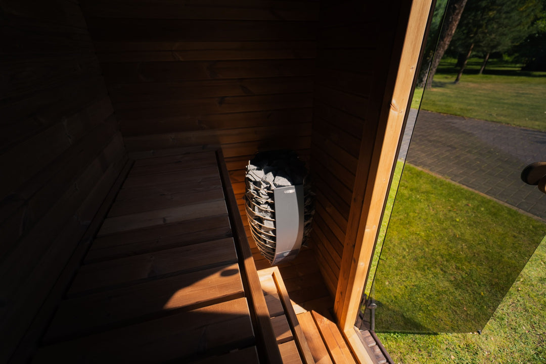 Ula Mini Outdoor Sauna exterior side view placed on grass in a wooded park setting with trees and pathway in the background.