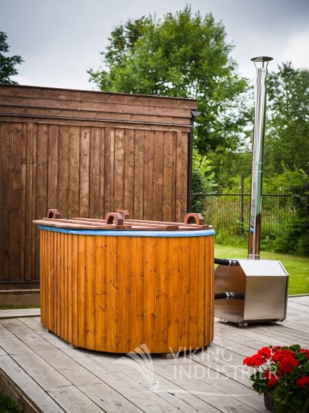 Covered Viking Industrier Ofuro hot tub with orange wooden cladding and external stainless steel stove beside a wooden shed.