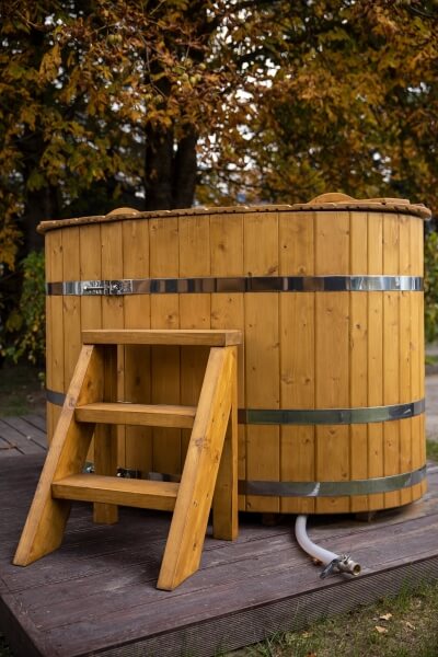 Viking Industrier oval cold tub with metal bands and wooden stairs in front, set outdoors on a deck with autumn trees in the background.