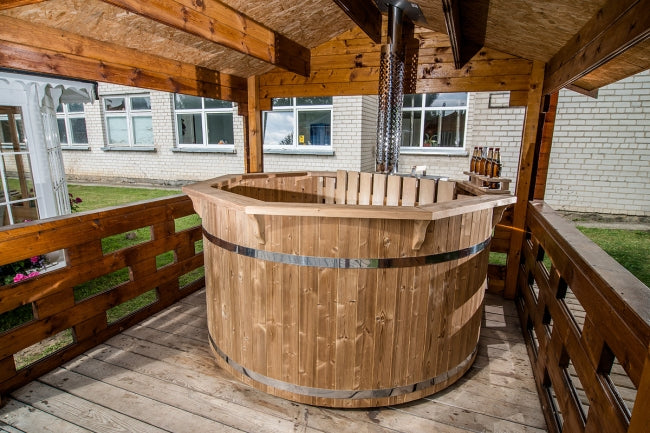 Viking Industrier Thermowood Hot Tub under a wooden roof structure on a wooden deck, with a brick building and windows in the background.