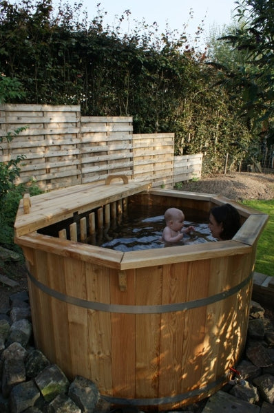 Viking Industrier Thermowood Hot Tub with a mother and baby bathing inside, placed in a private backyard with wooden fencing and greenery.