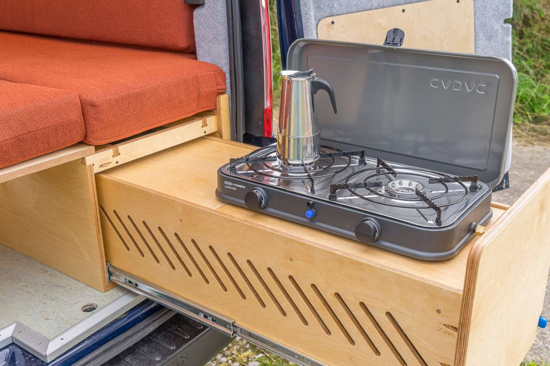 Campervan “Zawn” U-Berth Bench and Bed Unit slide-out kitchen drawer with double gas hob extended from rear of van, shown outdoors with rear doors open.