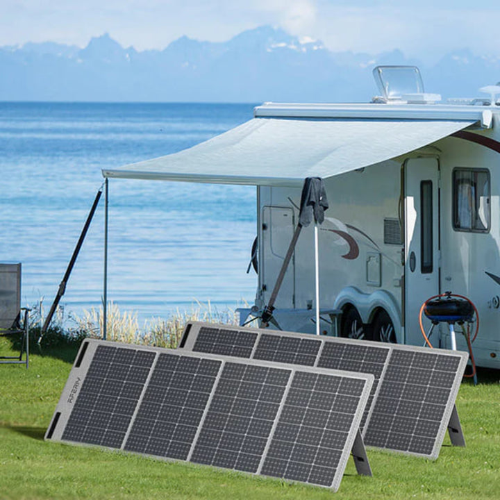 Two Aferiy solar panels set up on a green lawn in front of a white camper near a lake and mountains, under a wide canopy.