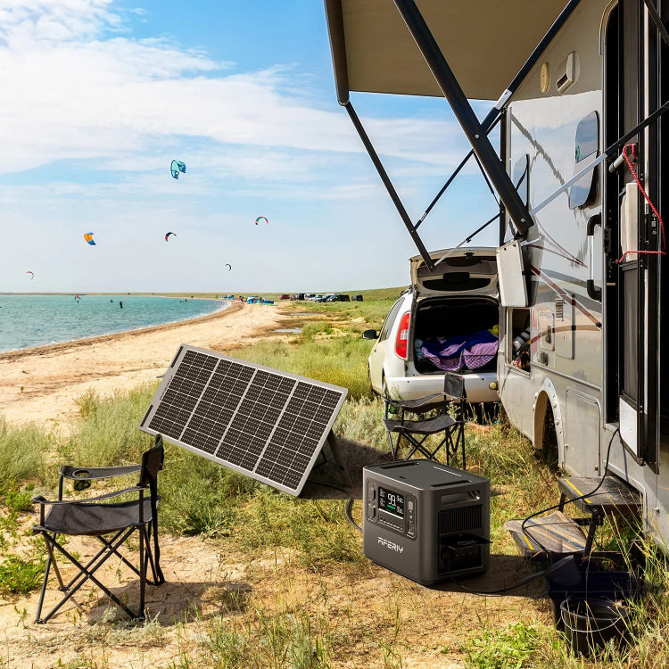 Aferiy P110 Solar Generator setup on a sandy beach beside a camper van, with a foldable solar panel facing the sun and power station placed on the ground.