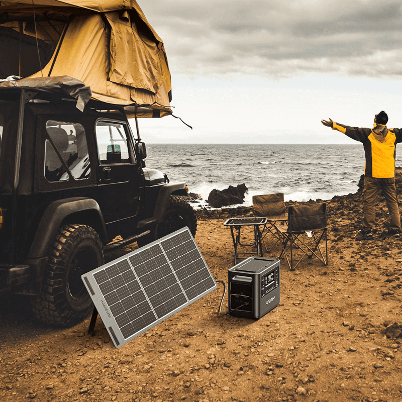 Aferiy P10 2400W Solar Generator Kit in a rugged coastal setting with an off-road vehicle and roof tent in the background, solar panel deployed.
