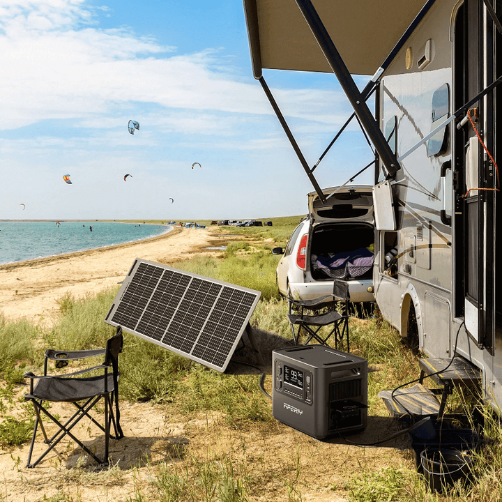 Aferiy P10 2400W Solar Generator Kit set up outdoors beside a camper van on a beach, solar panel angled toward the sun.