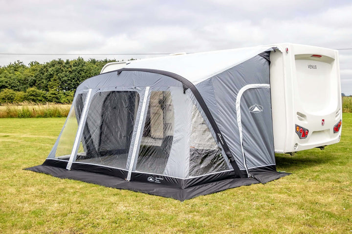 SunnCamp Swift Air 390 SC caravan awning with a large enclosed front section, clear window panels and grey fabric walls beside a white caravan.