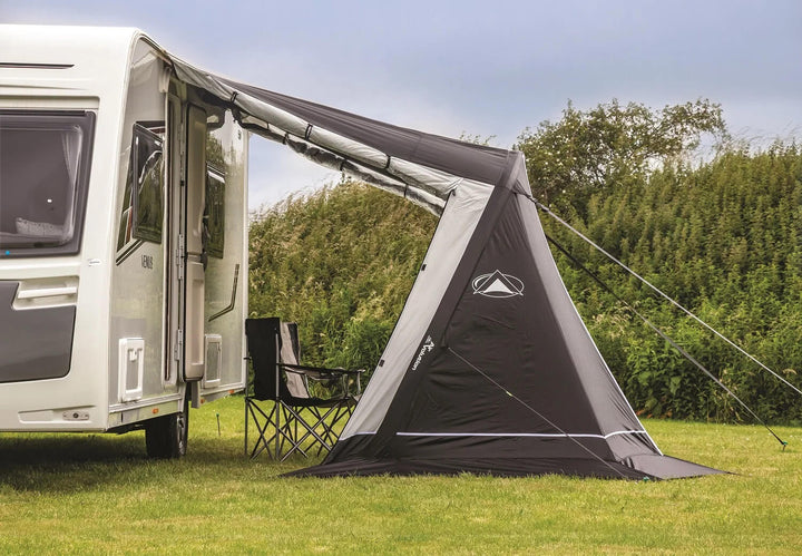 SunnCamp Swift Air 390 awning with a large covered entrance and two folding camping chairs underneath, attached to a white caravan, set on a grassy campsite under a clear, lightly cloudy sky.